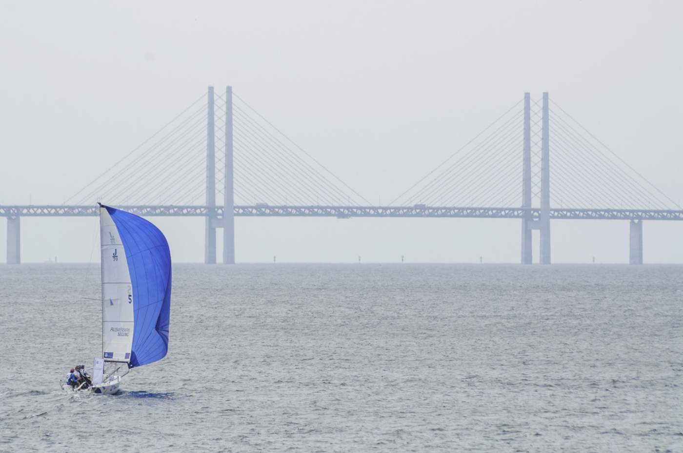 En liten besättning seglar under Öresundsbron mellan Sverige och Danmark